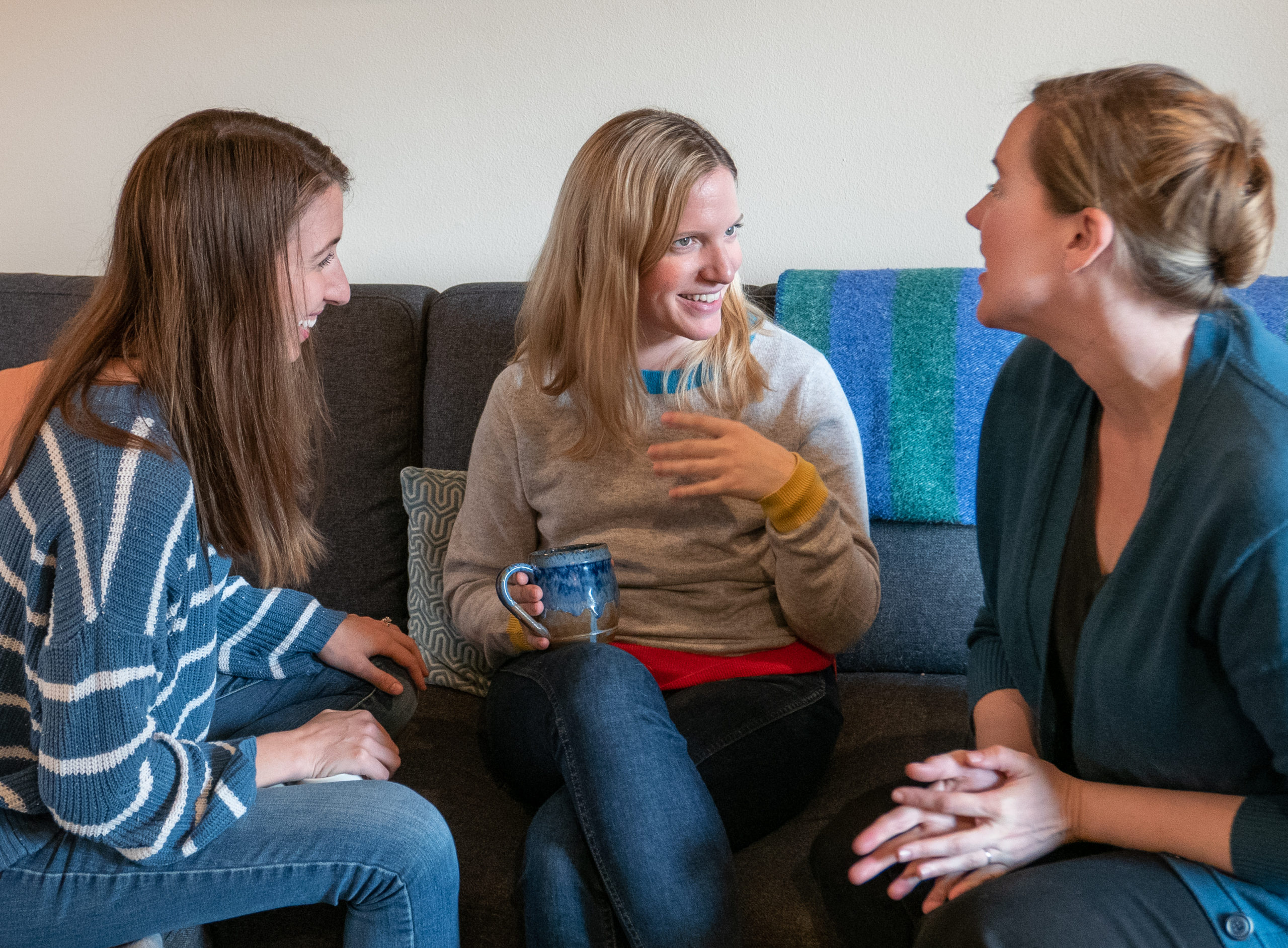 Photo of three women witting on a couch, facing one another, talking and smiling.
