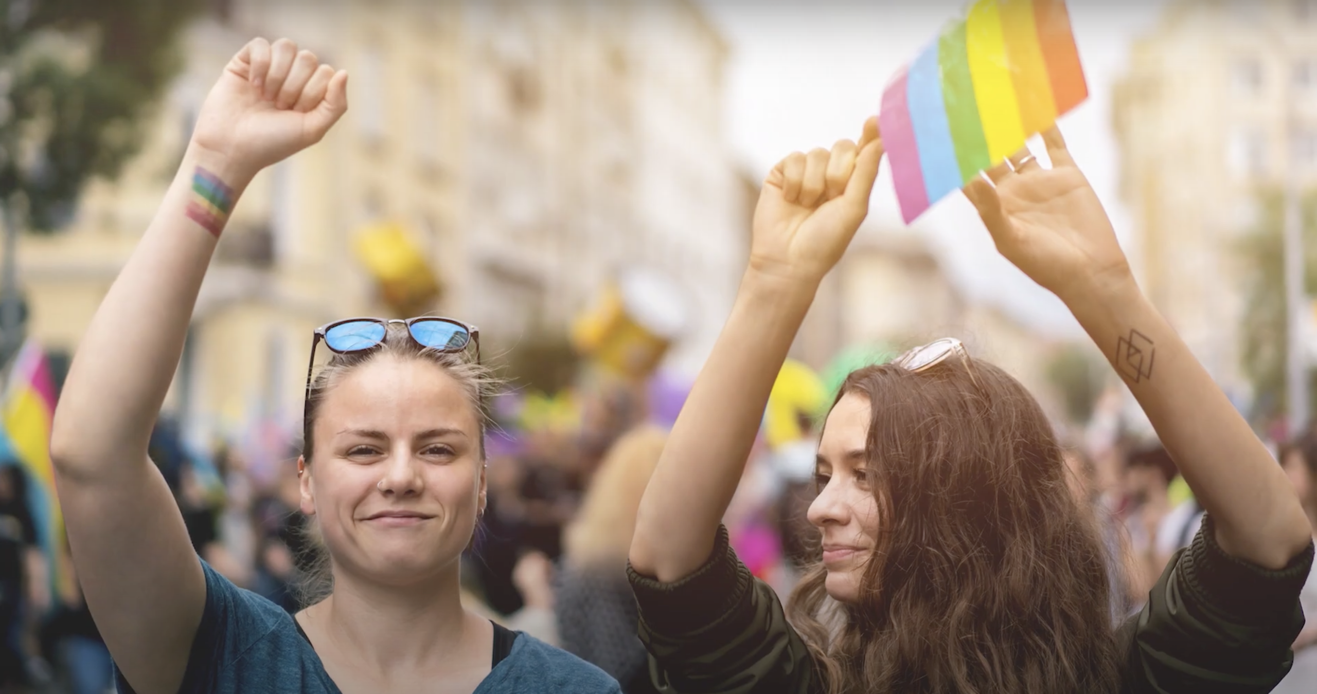 Photo of two individuals participating in a march with Pride flags.
