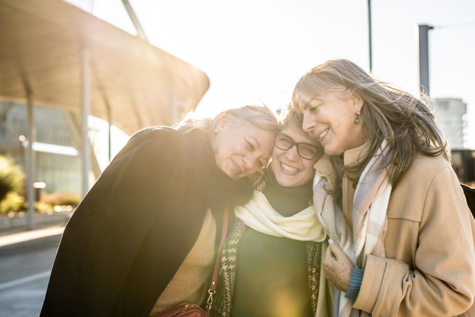 Three people huddle together smiling backlit by the sun