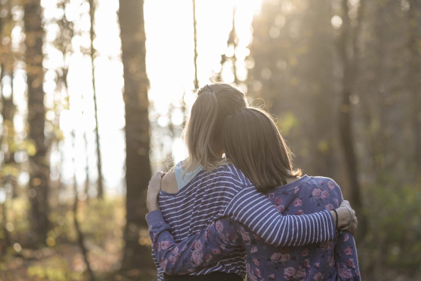 two people in woods seen from behind with arms around each other