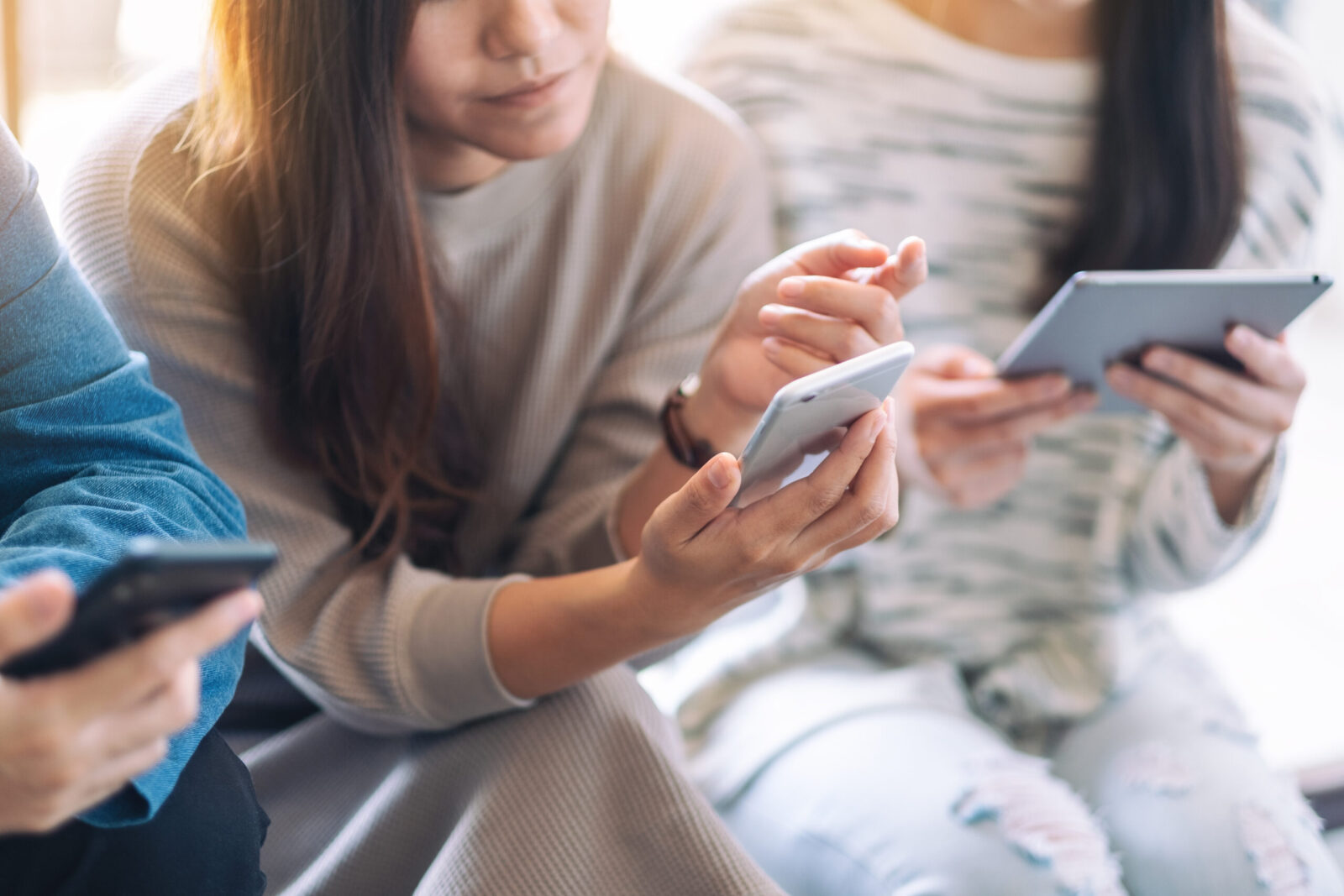 partial hands and bodies of three people looking at phones and tablets