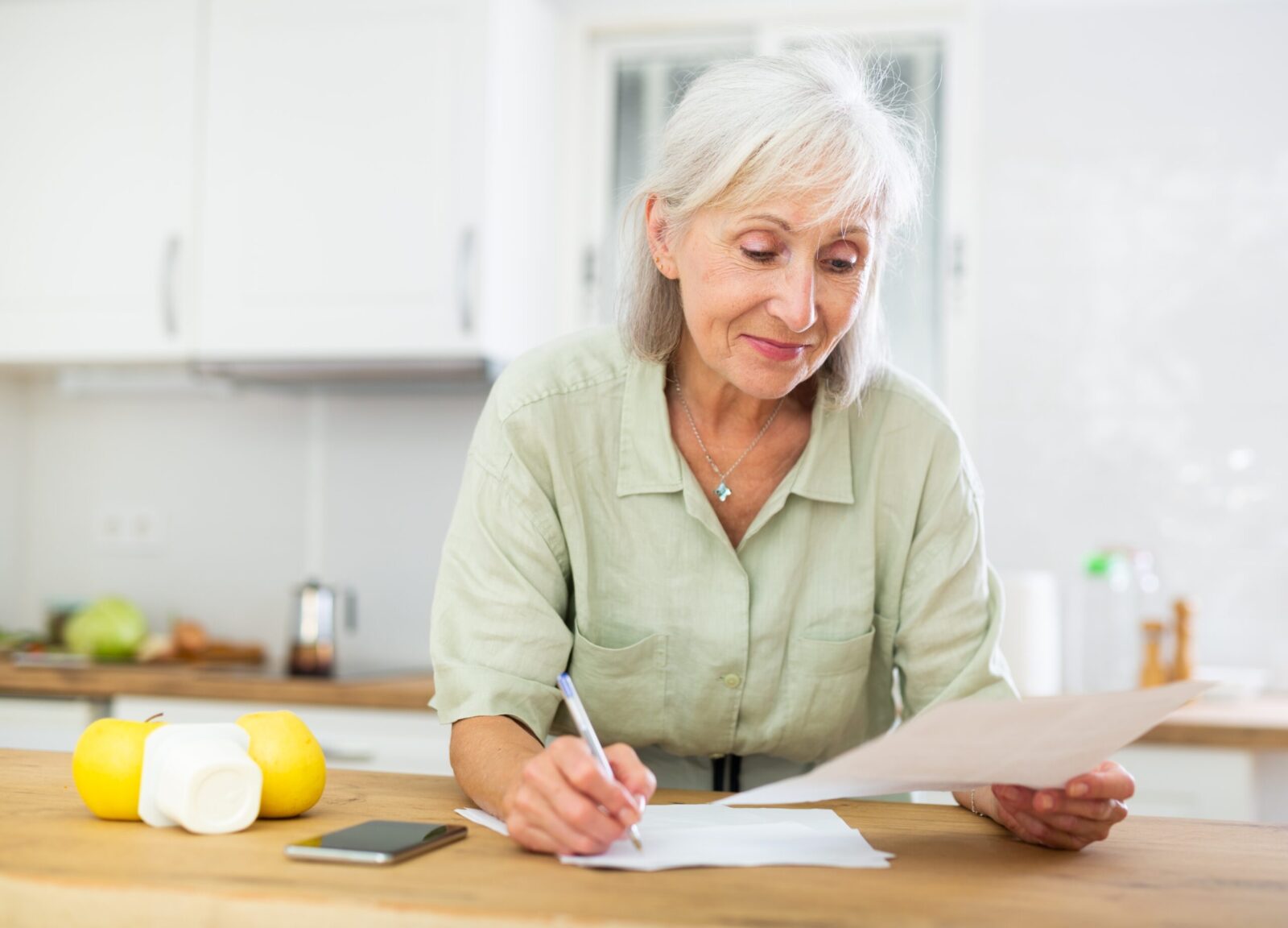 older woman looking at bills on table with slight smile
